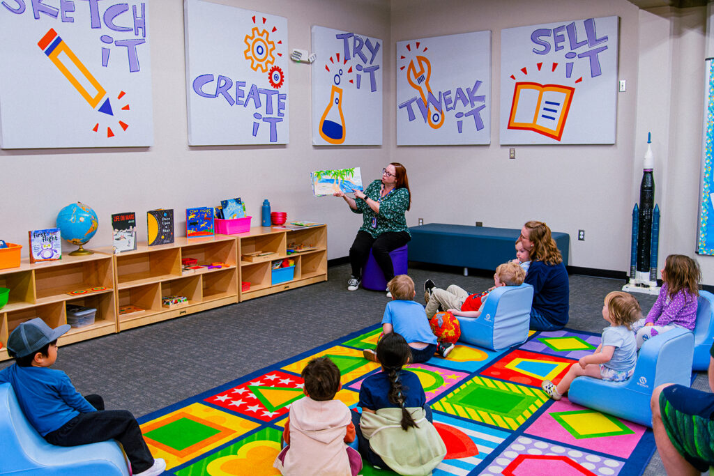 Educator reading a picture book to young children seated on a colorful rug in a classroom